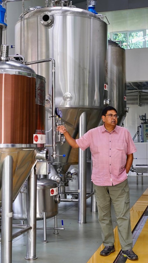 Mr. Ashok Patre standing beside the stainless steel fermentation tanks at Ratnagiri Estate
